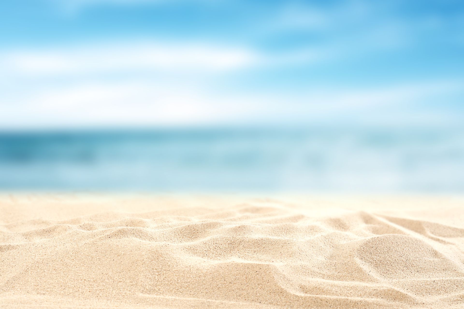 Nahaufnahme von feinem Sand mit unscharfem Meer und Himmel im Hintergrund